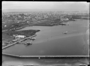 Tasman Empire Airways Ltd seaplane base, Mechanics Bay, Auckland, showing two seaplanes docked in front of TEAL building, with one seaplane taxiing into the base area