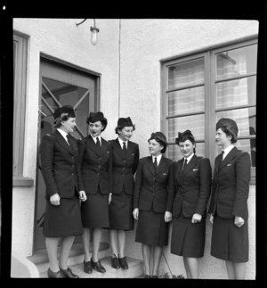 Tasman Empire Airways Ltd stewardesses, (l to r): Misses [Maynes?], Everand, Beckett, Woolley, Paterson and [Martin?] standing in front of the door of the TEAL building, Mechanics Bay, Auckland