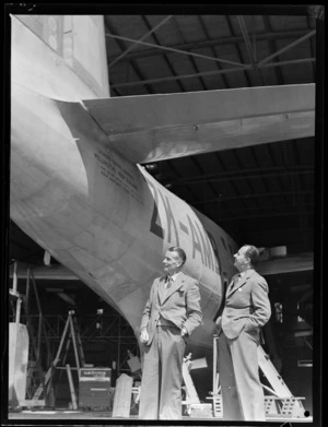 George Puddicombe and G Wells, near the tail end of a Tasman Empire Airways Catalina flying boat, ZK-AMB, in a hangar, Hobsonville, Auckland