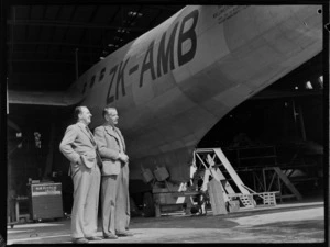 George Puddicombe and G Wells, near the tail end of a Tasman Empire Airways Catalina flying boat, ZK-AMB, in a hangar, Hobsonville, Auckland