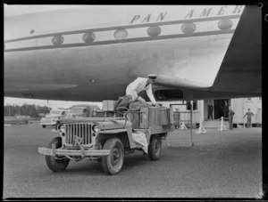 Unidentified male worker unloading luggage onto a Pan American World Airways Clipper Mandarin aircraft, Whenuapai, Auckland