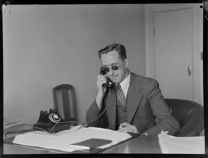 Portrait of an unidentified man sitting at his desk using the telephone, the Blind Institute Building, [Auckland?]