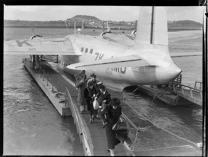 View of unidentified passengers disembarking on a gangway from TEAL Short Tasman flying boat ZK-AMD Australia, Mechanic's Bay, Auckland City