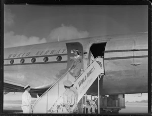View of Miss Hope Parkinson a Pan American World Airways (PAWA) Air Hostess descending boarding stairs from a PAWA Clipper passenger plane with unidentified men looking on, [Whenuapai Airfield, Auckland City?]