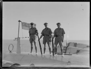 Group portrait of three unidentified RNZN soldiers at attention standing on top of TEAL Short S30 Empire Class flying boat 'Aotearoa' ZK-AMA in front of a NZ flag, Suva, Fiji