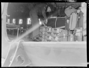 A view of an unidentified RNZAF Corporal securing boxes of tomatoes in the back of a Royal New Zealand Air Force Dakota aircraft at Whenuapai Airbase, Auckland