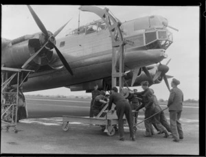 A group of unidentified men pushing a mobile crane at Whenuapai Airbase, Auckland, preparing to lift the propellor off the Avro Lincoln bomber aircraft Excalibur