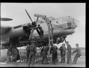 A group of unidentified men using a mobile crane to lift the propellor off the Avro Lincoln bomber aircraft Excalibur, at Whenuapai Airbase, Auckland