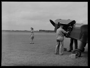 Two unidentified mechanics working on the engine of an aeroplane, as Emily Restall walks past, at Auckland Aero Club, Mangere, Auckland
