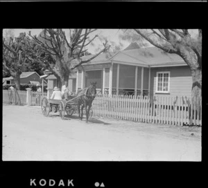 The Cook Islands Trading Company house with picket fence and unidentified people on a horse drawn wagon in front, Rarotonga, Cook Islands