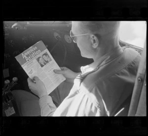 Inside a Dakota transport plane's cockpit with unidentified pilot looking at 'American Aviation' magazine for the 15th of June 1945, location unknown