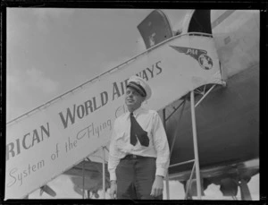 Portrait of Captain L Williams of Pan American Airways in uniform in front of a PAA Clipper Class Kathay passenger plane at Whenuapai Airfield, Auckland