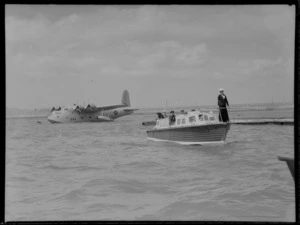 RNZAF (Royal New Zealand Air Force) Short Sunderland flying boat Mataatua NZ4103 moored at Mechanics Bay, passenger boat with members of NZ Navy and RNZAF heading to shore, Auckland