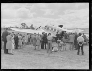 Opening of the Northland Air Service, Kaikohe, showing Kaikohe Town Board Chairman Mr G S Penney giving a speech, near an aircraft while a crowd looks on