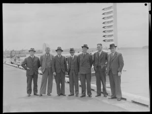 Group portrait of staff of Tasman Empire Airways Ltd, from left; FH Bass, Secretary, TA Barrow, Director, [J?]A Greenland, Director, AE [Dudder?], Chairman, [LJ?] White, Vice-Chairman, W Hudson, Director, G N Roberts, General Manager, standing on a quay, Auckland