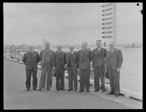 Group portrait of staff from Tasman Empire Airways Ltd, from left; FH Bass, Secretary, TA Barrow, Director, [J?]A Greenland, Director, AE [Dudder?], Chairman, [LJ?] White, Vice-Chairman, W Hudson, [Director?], and G N Roberts, General Manager, standing on a quay, Auckland