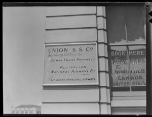 Sign reading 'Union SS (Steam Ship) Company, Booking Office For Tasman Empire Airways Limited (New Zealand to Australia), Australian National Airways Limited (New Zealand to USA and Canada) and All Other Principal Airways', includes another sign on the window reading 'Book Here for Honolulu, Canada, United States and Great Britain'