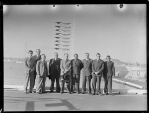 Arrival of Sir John Buchanan (3rd from left), with other unidentified men, Mechanics Bay, Auckland, including a sign behind them reading 'Sydney, Singapore, Calcutta, Hong Kong, Alexandria, Durban, London, Empire Flying Boat'