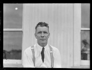 Portrait of H Mangham, Ground Engineer for Union Airways, in front of an unidentified building, Mangere Airport, Auckland