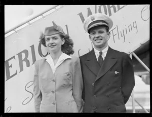 Portrait of Pan American Airways stewardess P Panasuk and an unidentified PAA pilot in front of plane boarding steps, Whenuapai Airfield, Auckland