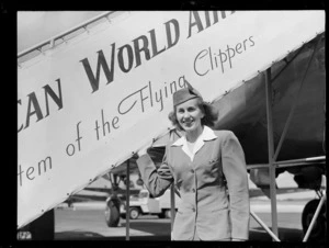 Portrait of an unidentified Pan American Airways stewardess in front of PAA plane boarding steps, Whenuapai Airfield, Auckland