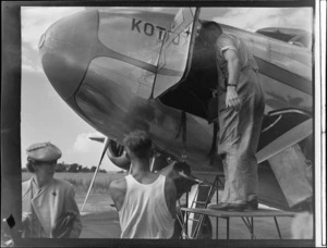 An unidentified woman passenger with ground crew unloading baggage from NZNAC Lockheed Electra 'Kotuku' twin engine passenger plane, Mangere Airport, Auckland