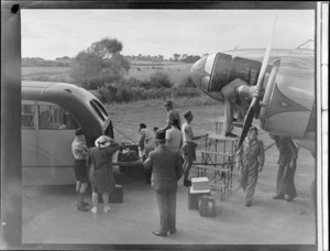 Unidentified passengers and ground crew transferring luggage from an NZNAC Lockheed Electra passenger plane on to a bus, Mangere Airport, Auckland
