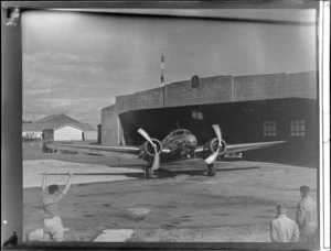 NZNAC Lockheed Electra 'Kaka' twin engine passenger plane in front of Union Airways of NZ hangar with unidentified ground crew, Mangere Airport, Auckland