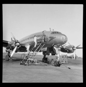 British Overseas Airways Corporation Lockheed Constellation aeroplane, on tarmac an an unidentified airport, including ground crew standing on external stairs alongside aircraft, Montreal, Canada