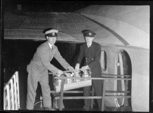Two unidentified Tasman Empire Airways crew member loading food onto aircraft, to serve to passengers during first flight to Sydney