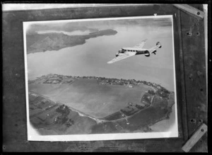 Photomontage of a Union Airways Lockheed L10 Electra aeroplane, ZK-AFD, flying over Whangarei Airport, Onerahi, Whangarei, made from photographs taken by Leo White