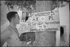 J T Needham looks at Silver Fern sign superimposed over German sign at Sora, Italy, World War II - Photograph taken by George Kaye