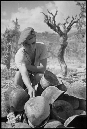 P Dentice examines tin helmets found in destroyed German quartermaster's stores near Sora, Italy, World War II - Photograph taken by George Kaye