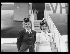 Betty Park, left, and Margot Umphelby, Trans Australia Airlines stewardesses, standing alongside a Douglas DC4 Skymaster aeroplane, after special charter flight to New Zealand