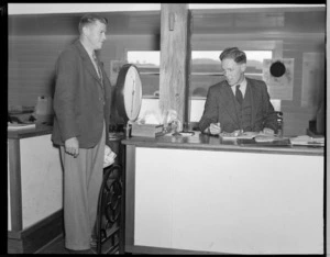 Unidentified NZNAC (New Zealand National Airways Corporation) booking agent, weighing in an unidentified passenger at a Wellington Office