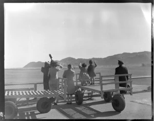 Unidentified group, including two children, waving goodbye to a NZNAC (New Zealand National Airways Corporation) aircraft, Rongotai airport, Wellington