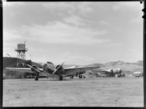New Zealand National Airways Corporation Lockheed Electra 'Kahu', ZK-AGJ, twin engine passenger plane, at Rongotai Airport, Wellington, also showing traffic control tower, another plane and refueling trailer