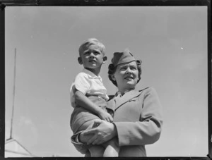 Tasman Empire Airways Ltd stewardess holding a small boy, both unidentified, [at a photoshoot for an advertising campaign?], Mechanics Bay, Auckland