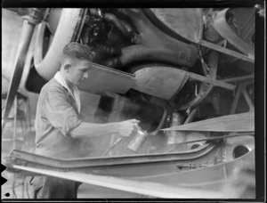 An unidentified man spray-painting an aeroplane during reconversion to civil aviation, New Zealand National Airways Corporation workshop, Milson, Palmerston North