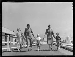 Tasman Empire Airways Ltd stewardesses walking with three unidentified children, [during a photoshoot for an advertising campaign?], on the wharf at Mechanics Bay, Auckland