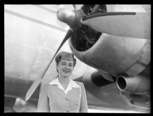 Portrait of Miss Betty Fleming, a PAA stewardess in front of a passenger plane, Whenuapai Airfield, Auckland