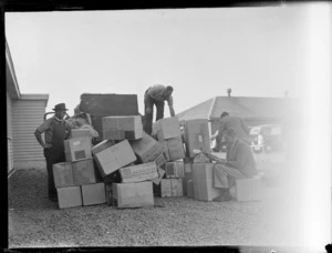 View of unidentified men loading a shipment of nylon stockings for H A Tuck & Co Ltd, 171 Albert Street Auckland, on to a truck from a PAA Clipper class passenger plane, Whenuapai Airfield, Auckland
