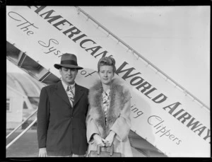 Portrait of Mr & Mrs Albert and Reynal Skelton in front of a PAA Clipper passenger plane boarding ramp, Whenuapai Airfield, Auckland