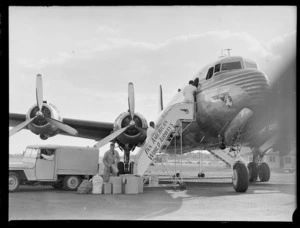 View of PAA NC-88948 'Clipper Westward Ho' passenger plane being unloaded by unidentified ground crew, Whenuapai Airfield, Auckland
