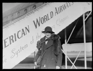 Portrait of Miss Annie Lee with a fox fur stole in front of a PAA Clipper passenger plane gangway, Whenuapai Airfield, Auckland