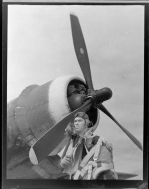 Portrait of Squadron Leader D Greig in flight gear standing in front of his plane, Ardmore Aerodrome, Auckland Region