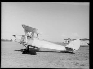 Tiger Moth aircraft (ZK-AID), at [Whenuapai Airbase?], Auckland, including an unidentified man and an Autocrat monoplane (ZK-AOB) in the background