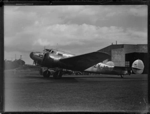 New Zealand National Airways Corporation (NZNAC) Lockheed Electra aircraft, 'Kahu' (ZK-AGJ) at Mangere Aerodrome, Auckland, showing 'Kahu' sitting in front of the Union Airways of New Zealand Ltd hangar