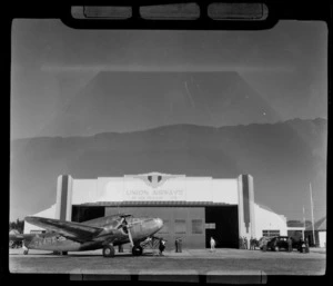 NZ NAC passenger plane ZK-AHX 'Karoro' and unidentified people in front of Union Airways hangar, Taieri Airport, South Dunedin, Otago Region