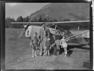 Portrait of Mr E F Harvie with his four children in a field in front of Auster J-1B Autocrat ZK-AOB plane, Queenstown, Otago Region